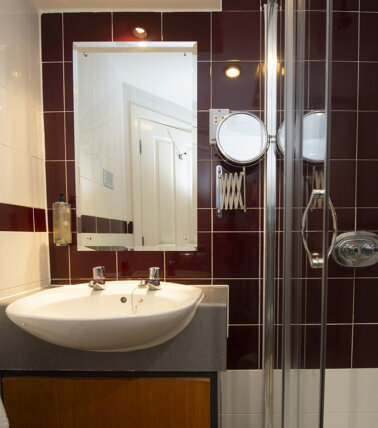 Hotel ensuite bathroom with maroon tiles and shower
