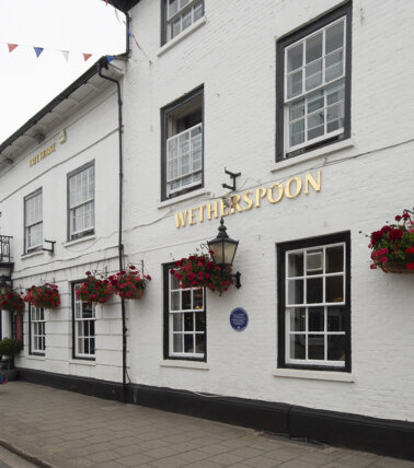 Exterior view of The Catherine Wheel Wetherspoon pub with white brick walls and hanging flower baskets