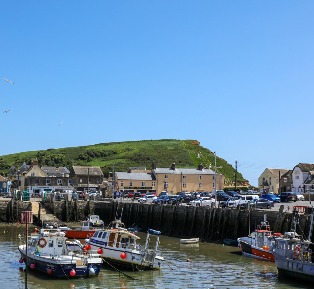 A view of the pretty harbour at West Bay with Pleasure boats and fishing boats at moorings with low tide in a sunny day.