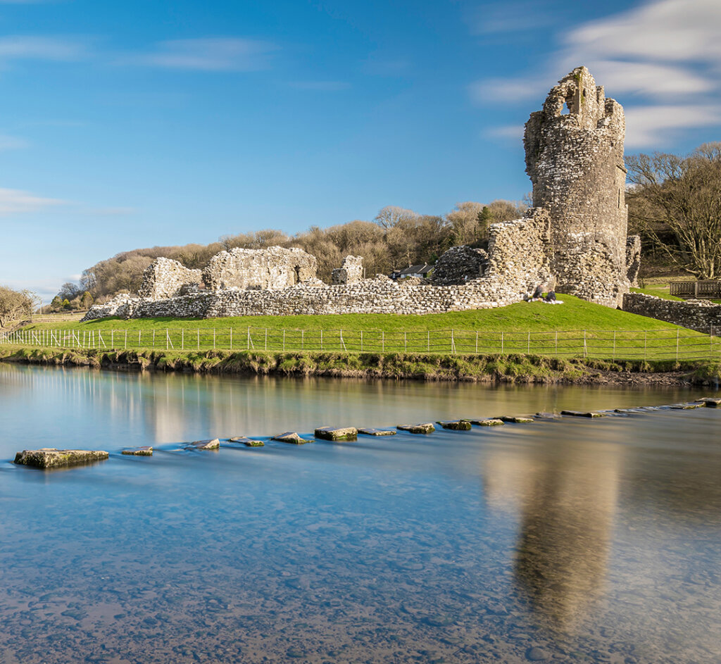 Ogmore Castle, a ruined Norman castle near Bridgend, south Wales. The castle is reflected on the smooth water of the river Ogmore.